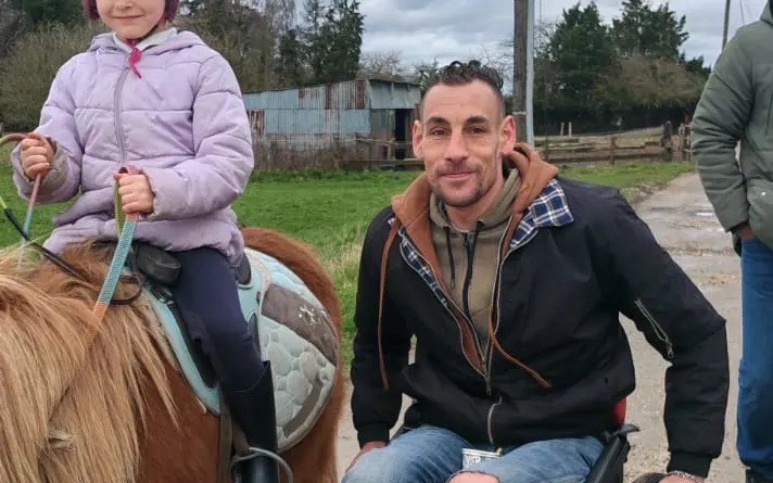Axel Broutin souriant auprès d'une enfant sur un poney, un moment de complicité