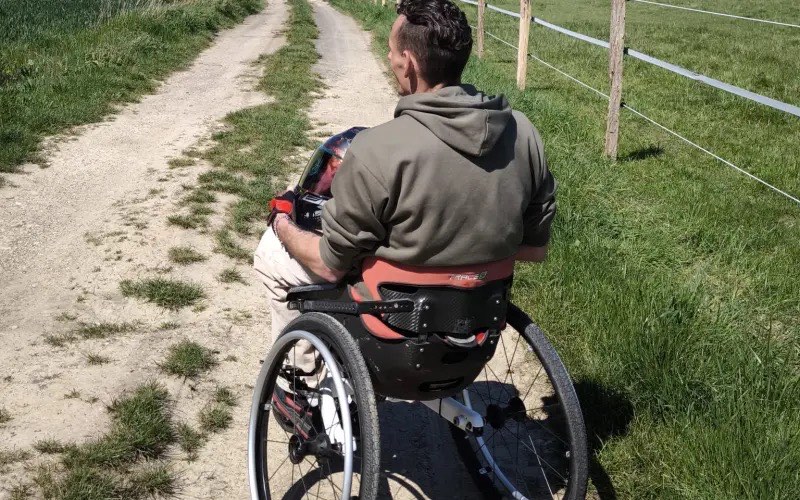 Axel Broutin dans son fauteuil tout-terrain sur un chemin de campagne, de dos